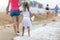 Mother and daughter girl walking together on sand beach in sea water in summer with bare feet in warm ocean waves
