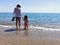Mother and daughter hand in hand with bare feet in front of the beach with copy space