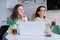 Mother and daughter at home in kitchen sitting at table with laptop computer