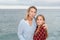 Mother and daughter hugged and happy looking at the camera next to the sea. Mother sends a kiss to the camera