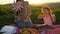 Mother and daughter on a picnic on a hill in the summer at sunset.