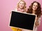 Mother and daughter on pink background showing blank board