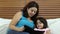 Mother and daughter reading an electronic book in the bedroom