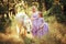 Mother and daughter in similar lavender dresses are petting a unicorn horse. Summer meadow