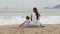 Mother with a daughter sitting with his back to the camera on the sandy beach.