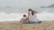 Mother with a daughter sitting with his back to the camera on the sandy beach.