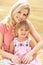 Mother And Daughter Sitting On Straw Bales In Harv