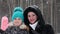 Mother and daughter smile and wave hands during snowfall in winter park