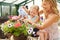 Mother And Daughter Watering Plants In Greenhouse