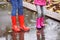 Mother and daughter wearing rubber boots splashing in puddle on rainy day, focus of legs