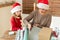 Mother and daughter wearing santa hats having fun wrapping christmas gifts together in living room. Candid family christmas time.