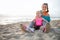 Mother and daughter in workout gear sitting together on beach