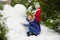 Mother with daughter of younger school age build a snowman in the park.