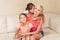 Mother and daughters girls hugging together on couch. Young Caucasian woman playing with children sisters at home. Family mom and