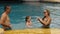 The mother and father with little daughter have fun in the pool. Mom and dad plays with the child. The family enjoy