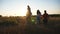 Mother and father with two little children going among meadow. Young couple of parents with small kids walking through