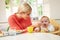 Mother Feeding Baby Sitting In High Chair At Mealtime