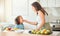 Mother feeding child vegetables while cooking together in the kitchen. Mom and daughter spending time together at home