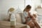 Mother feeding her little baby at home, focus on breast pump with milk. Healthy growth