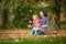 Mother and girl having fun under tree with autumn leaves in the park, blond cute curly girl, happy and young family