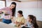 Mother with girls indoors at home, preparing fruit smoothie drink.