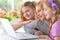 Mother and girls sitting at table and using laptop