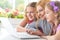 Mother and girls sitting at table and using laptop