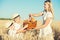 Mother gives children a basket with fresh bread and milk. A picnic on a wheat field.