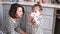 Mother gives her daughter a cup of water, little girl drinks, mom is smiling on the kitchen