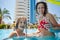 Mother with glass of beverage and daughter hide under umbrella