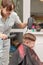 Mother with a hairdryer in her hand in a light blue dress is doing her son`s hair at home during the second period of quarantine.