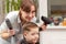 Mother with a hairdryer in her hand in a light blue dress is doing her son`s hair at home during the second period of quarantine.