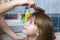 Mother hand with brush combing long fair hair of cute child girl after bath on blurred interior background