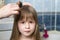 Mother hand with brush combing long fair hair of cute child girl after bath on blurred interior background
