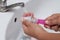 Mother hand washing baby plastic nipple on white sink