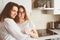 Mother having breakfast with teen daughter at home in modern white kitchen