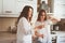 Mother having breakfast with teen daughter at home in modern white kitchen