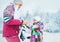 Mother helping her little daughter wearing warm gloves during snowy forest walking