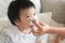 Mother helping to blow asian child`s nose with paper tissue. Sea