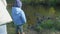 Mother and her child sit near river watching and feeding ducks