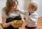 Mother and her daughter having fun and playing. Little child is feeding her mother with salad