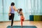 Mother and her daughter in preschool age practicing balancing yoga pose with one leg up together in the gym