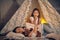 Mother and her daughter are in a teepee tent with some pillows. Happy family.