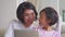 Mother and her daughter use laptop on couch