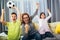 Mother and her kids raising arms and screaming while watching football match and celebrating goal