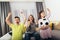 Mother and her kids raising arms and screaming while watching football match and celebrating goal at home