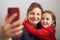 Mother with her little daughter making video call using mobile phone. Woman and little girl talking with relatives. Cheerful