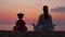 Mother and her little daughter meditate by the sea or ocean shore while admiring the sunset.