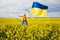 Mother with her son on shoulders with large satin flag of Ukraine among blooming yellow rapeseed field