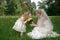 mother in her wedding dress holding a wedding bouquet with little daughter in wedding dresses. Outdoors summer portrait